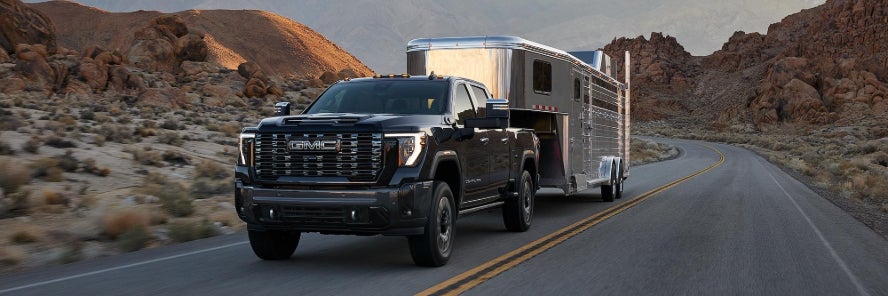 A black GMC Sierra towing a trailer while it drives down a desert road.