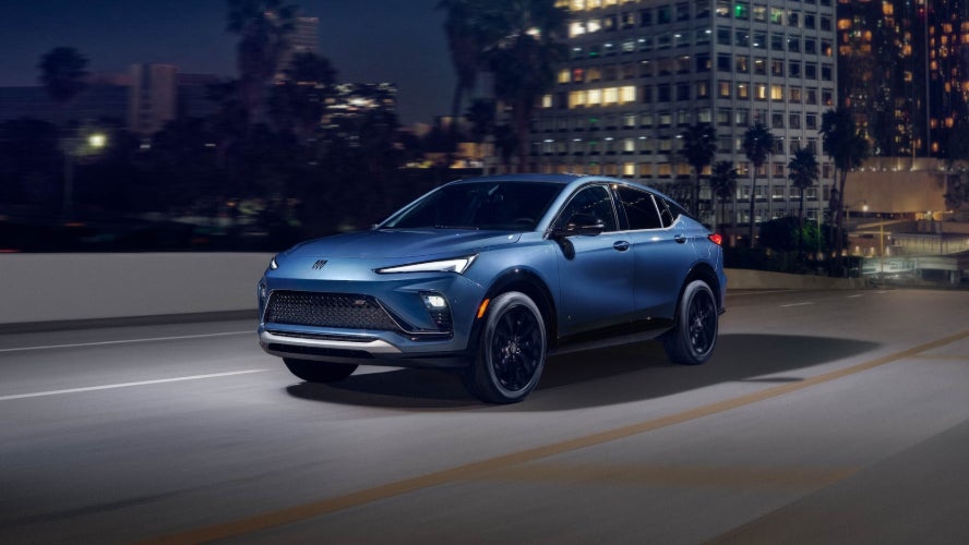 A blue Buick Envista driving over a bridge in a city at night.