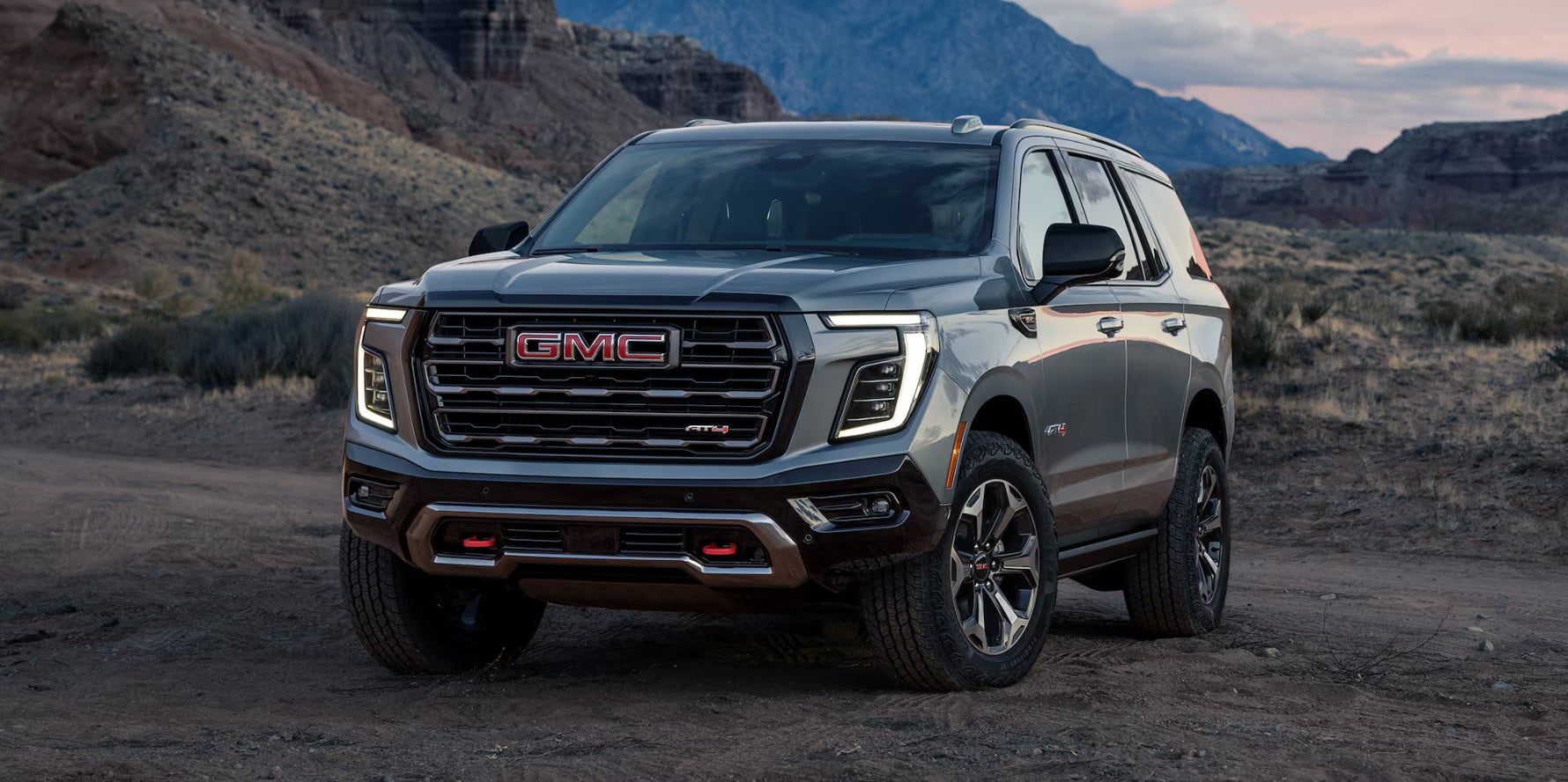 A light blue GMC Yukon parked on a dirt road in a mountainous area.
