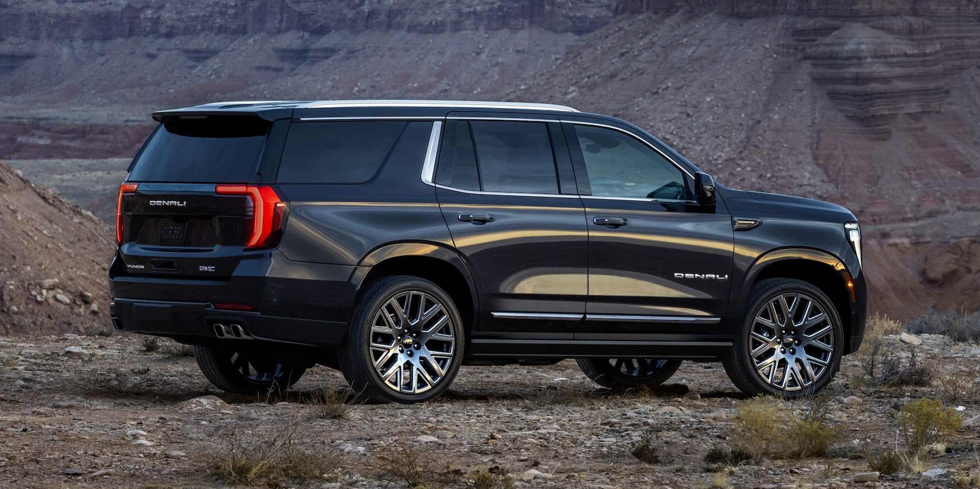 A black GMC Yukon off-road in a desert plateau.