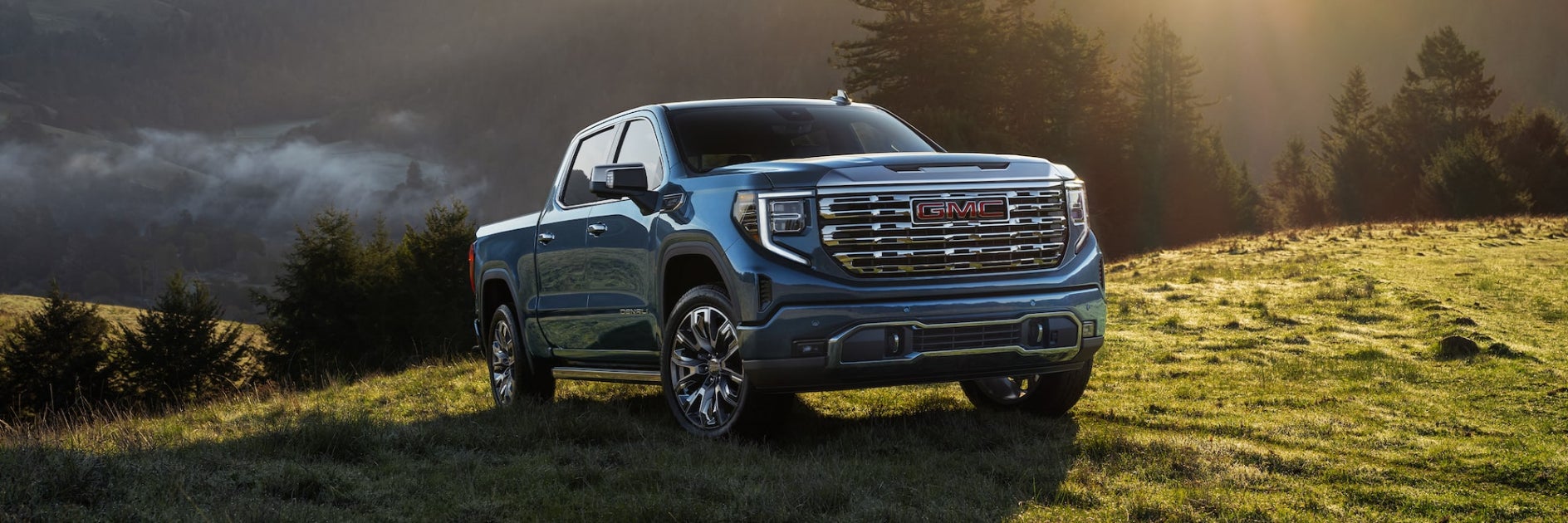 A blue GMC Sierra 1500 on the top of a grassy hill.