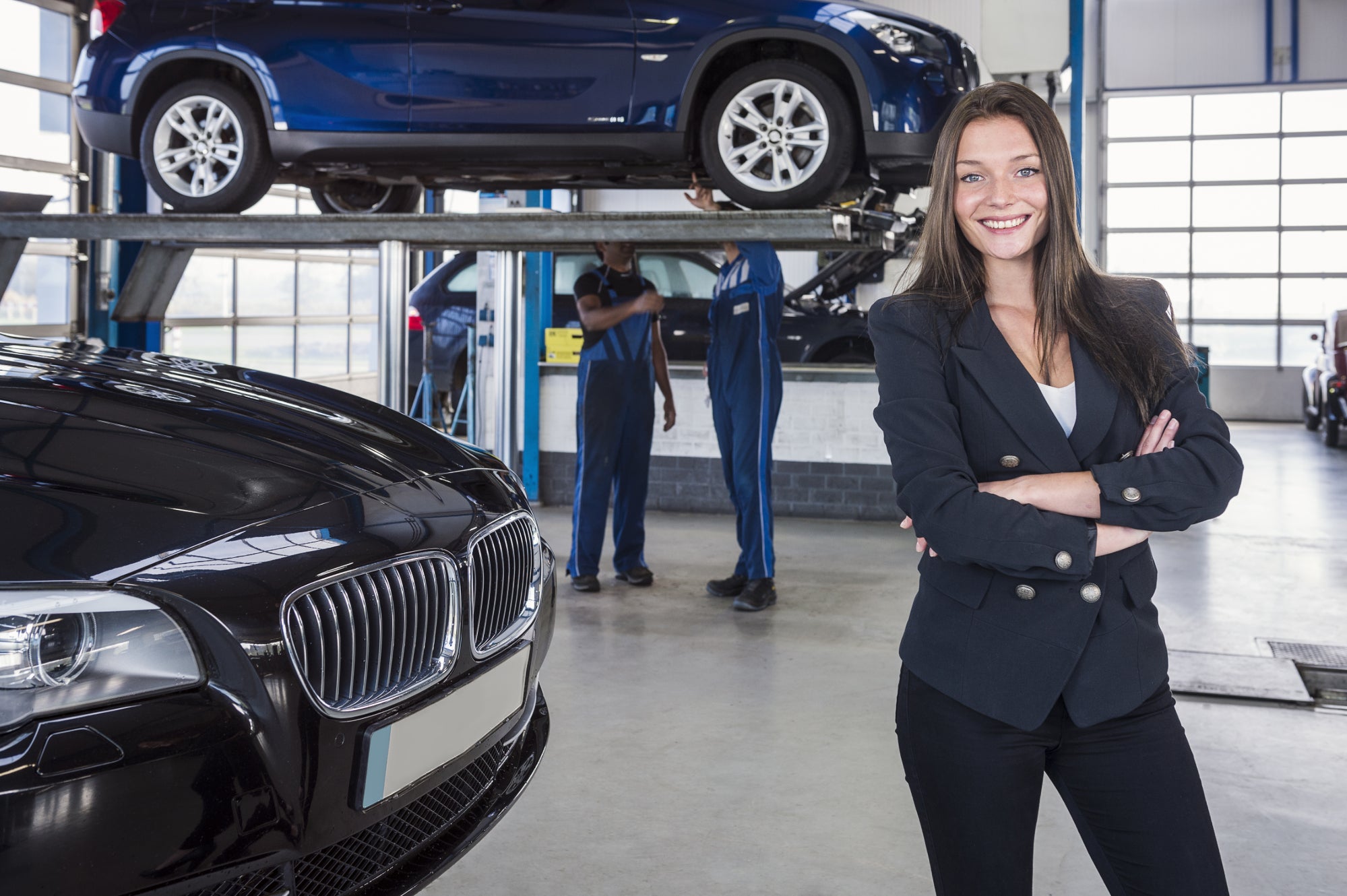 A woman smiling as car technicians work on vehicles in the background.